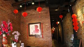A hotel reception area with a brick wall, a chandelier, red lanterns, and a framed sign. - Ban Loong Hotel (Ipoh)