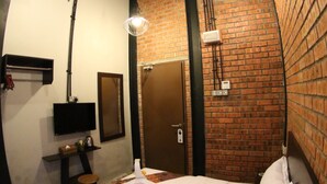 A room with a bed, a television, a mirror, and a brick wall. - Ban Loong Hotel (Ipoh)