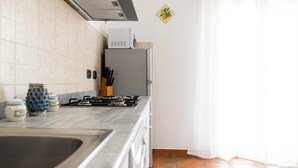 A kitchen with a gas stove, a refrigerator, and a microwave on top. There are cabinets and a sink. - Apartment in villa wi fi 200 meters from the beach UA (Alcamo)