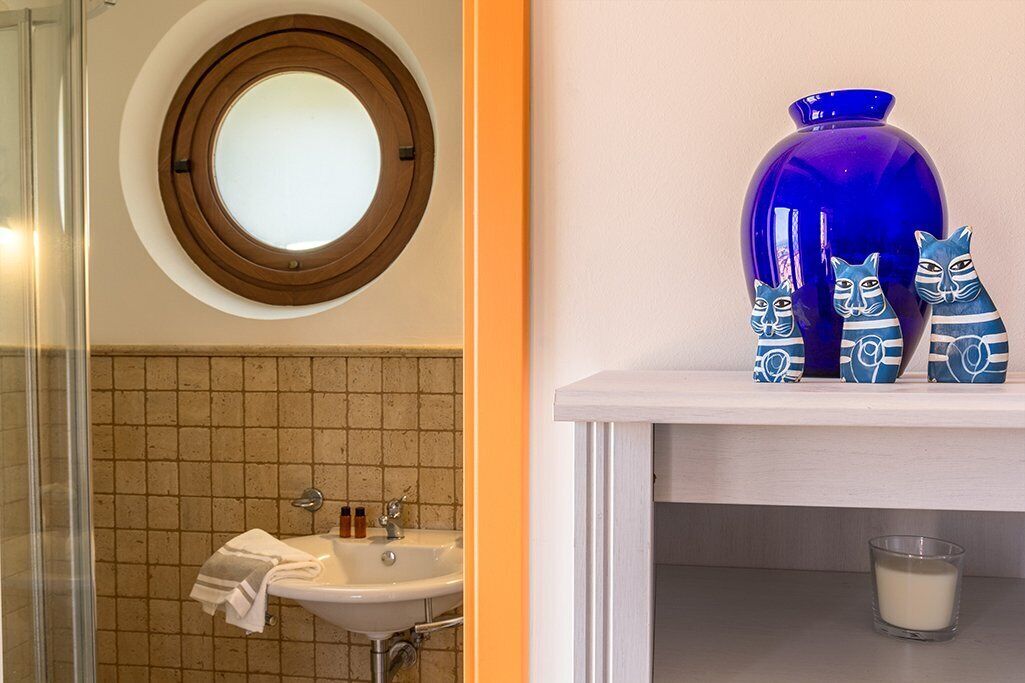 A bathroom with a round mirror, a sink, and a shelf with decorative items.