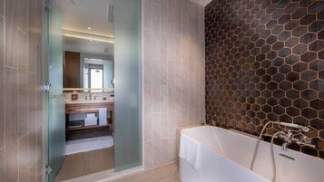 A modern bathroom with a glass door leading to a shower area, a large bathtub with a showerhead, and a hexagonal patterned wall.