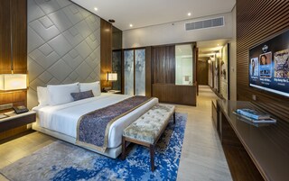 Una habitación de hotel moderna con una cama grande, mesitas de noche, un banco, un televisor y una obra de arte colgada en la pared.