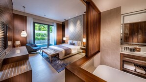 Een moderne hotelkamer met een bed, nachtkastjes, een bureau, een stoel, een badkamer met een badkuip en een grote spiegel.