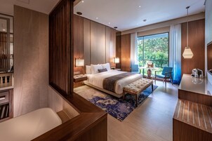 Habitación de hotel moderna con una cama grande, un escritorio, una silla y un balcón con vistas a zonas verdes.