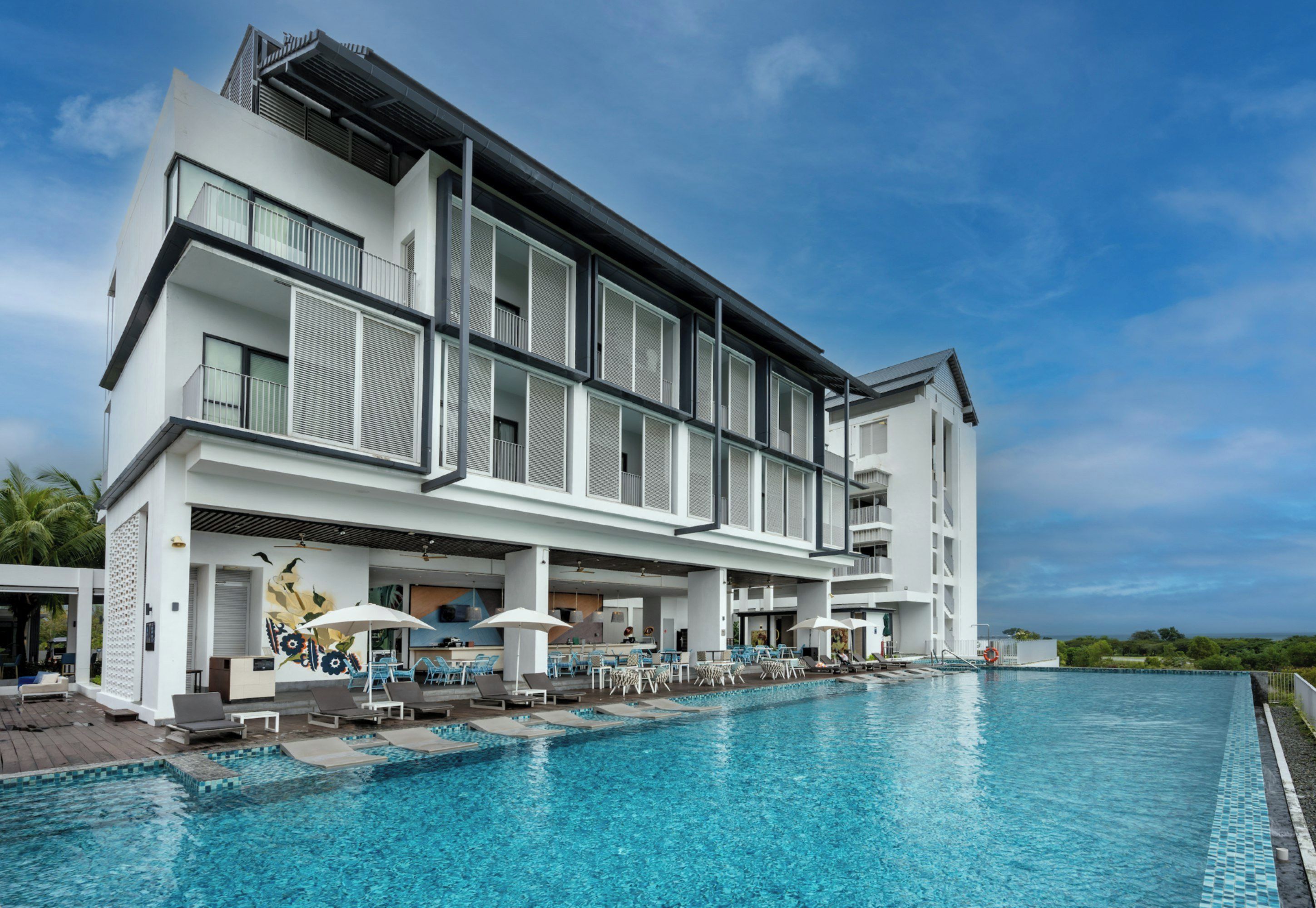 A modern hotel with a swimming pool, outdoor seating, and a view of the ocean.