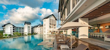 Un hotel moderno con una amplia piscina, tumbonas y zonas de estar al aire libre.