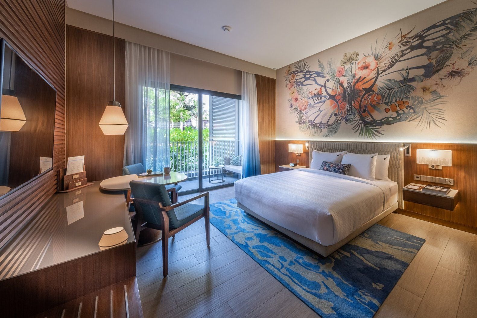 A hotel room with a bed, a desk, a chair, a large window, and a wall mural.