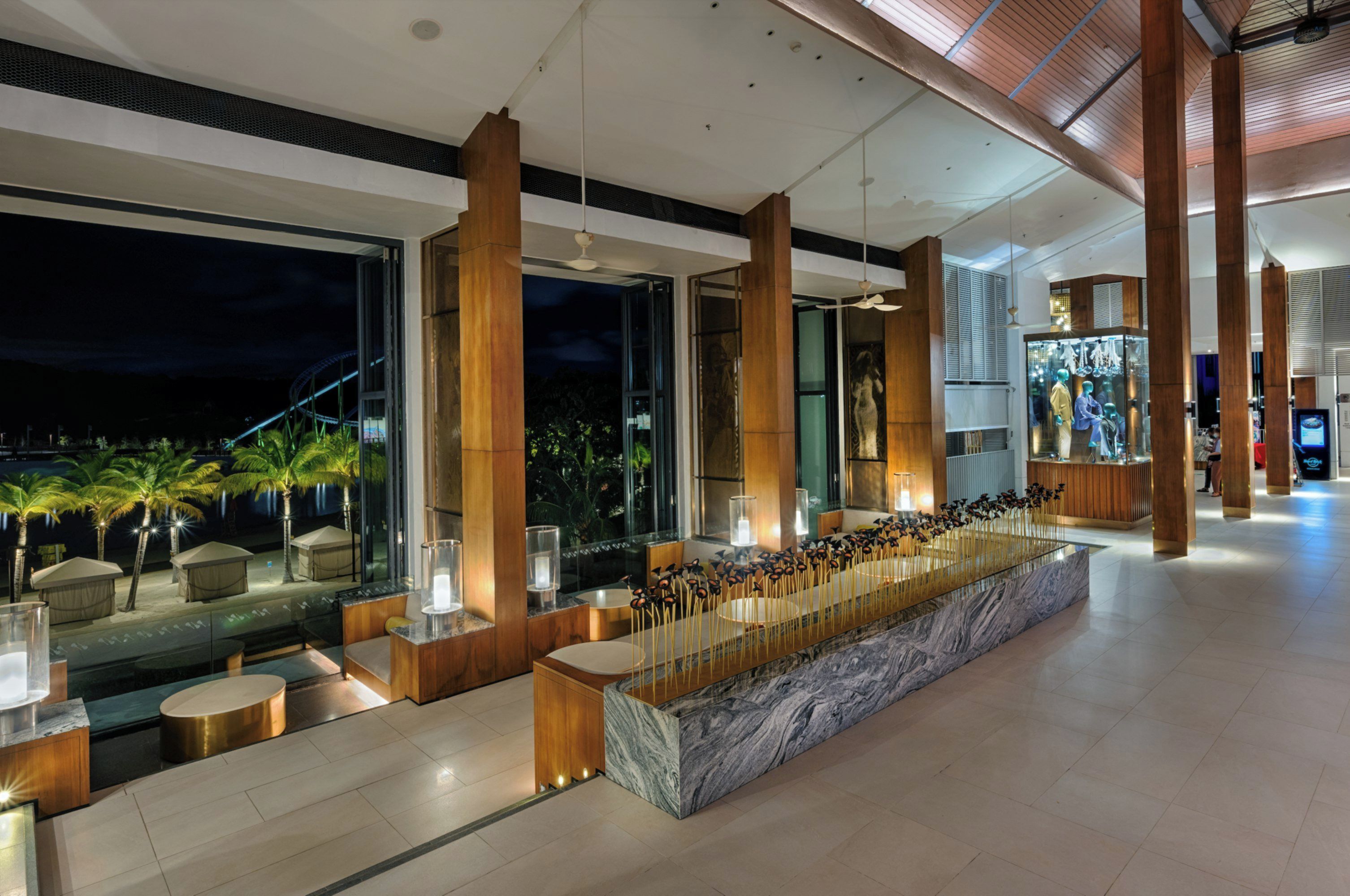 A modern hotel lobby with a long reception desk, large windows, and a view of palm trees outside.