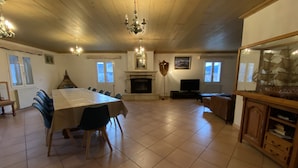 Un salon spacieux avec une grande table à manger, de nombreuses chaises, une cheminée, un téléviseur et une maquette de bateau décorative.