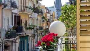 Una hilera de edificios tradicionales con balcones, una imponente aguja de iglesia al fondo y un objeto esférico en la barandilla de un balcón.
