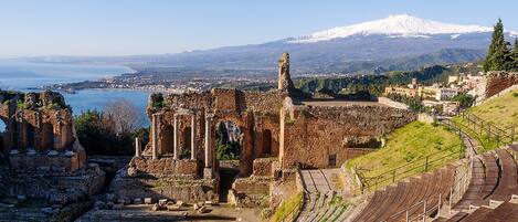 Ruinas antiguas con un estadio y una montaña nevada al fondo.