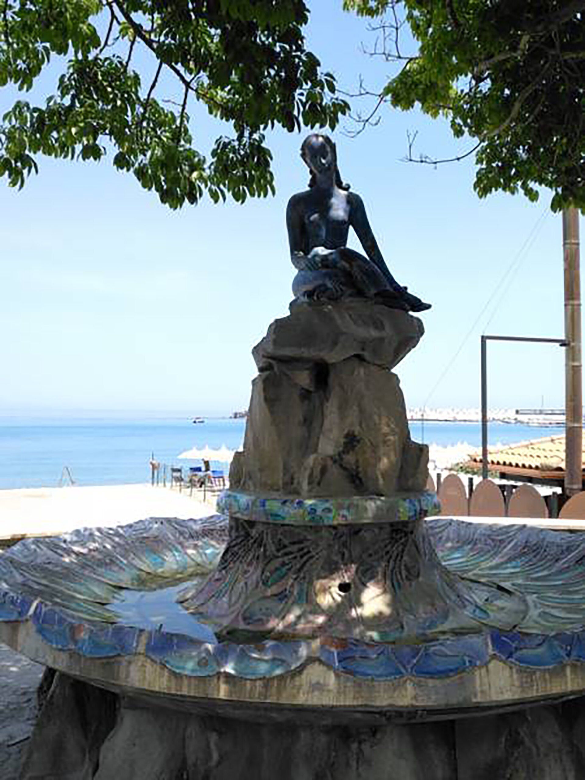 Una estatua de una figura sentada sobre una roca, rodeada por una piscina decorativa con mosaicos.