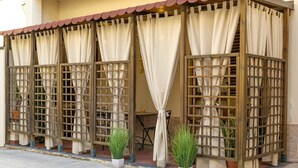 Un espacio de estar al aire libre cubierto, con paneles de celosía de madera y cortinas color crema.