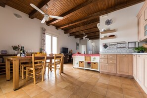 Eine geräumige Küche mit Holzausstattung, ein Essbereich mit Holztisch und -stühlen sowie ein Deckenventilator.