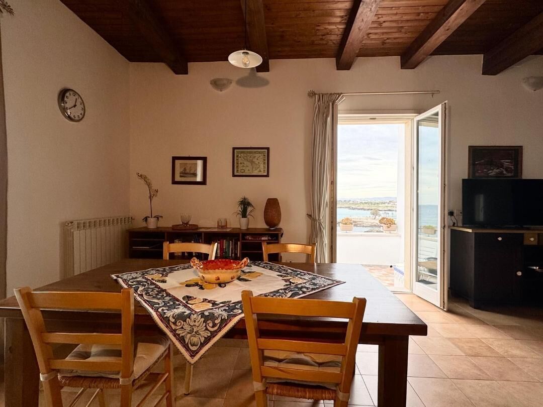 Ein Essbereich mit einem Holztisch, Stühlen und Blick auf das Meer durch eine offene Tür.