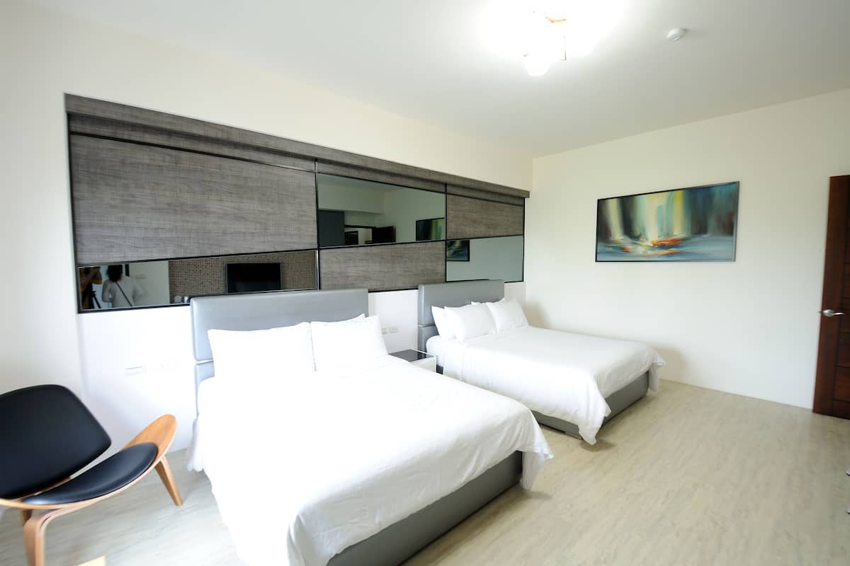A hotel room with two beds, a chair, a large mirror, and a painting on the wall.
