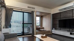 A modern living room with a sofa, a coffee table, a TV, and a sliding glass door leading to a balcony. - Jophina B&B (Donggang)