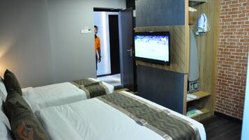 A hotel room with two beds, a TV mounted on the wall, a shower area, and a brick wall.