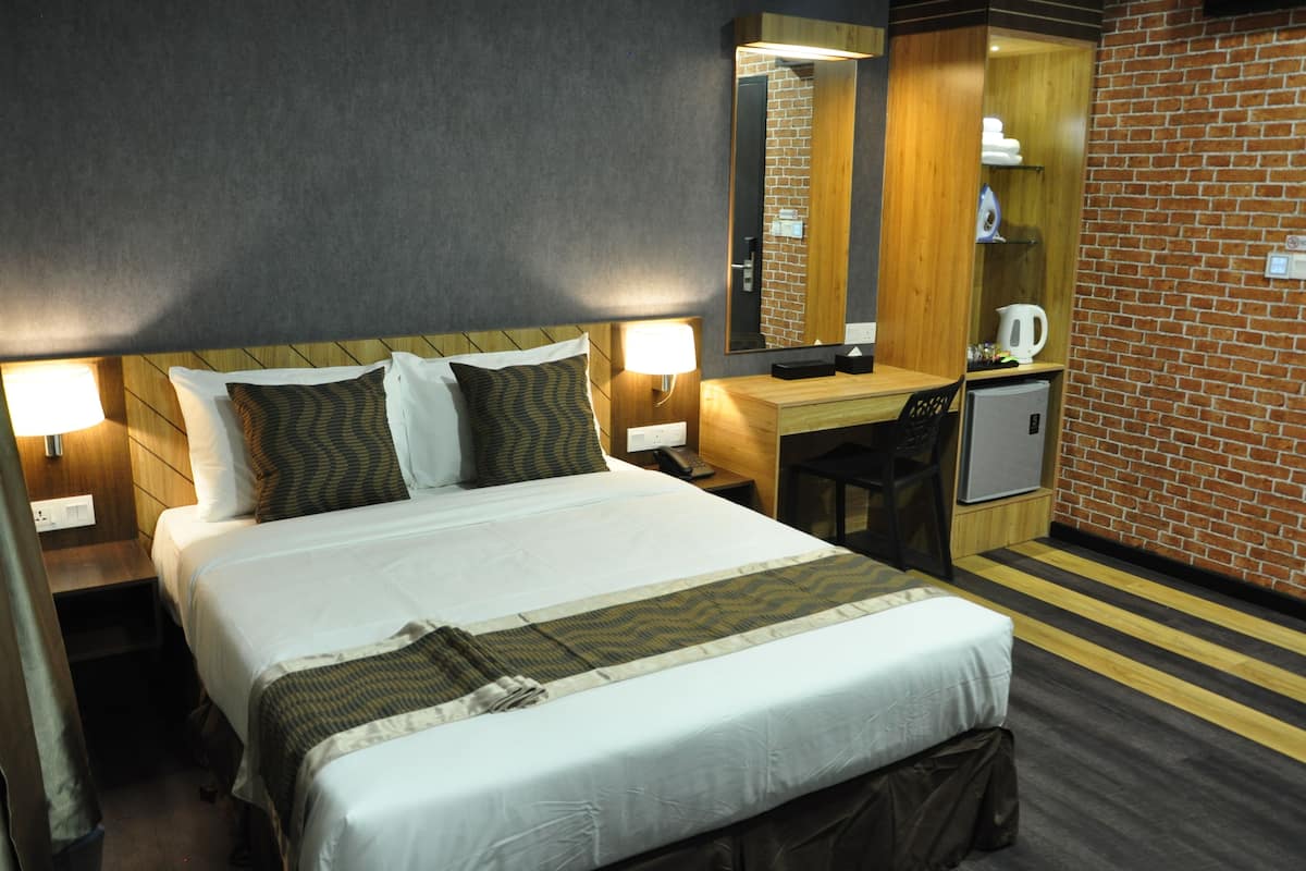 Une chambre d’hôtel avec un grand lit, un bureau, une chaise, un petit réfrigérateur et un miroir.