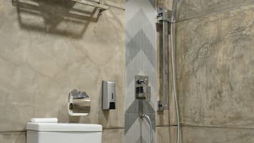 A bathroom with a toilet, a towel rack, a shower, and a towel dispenser.