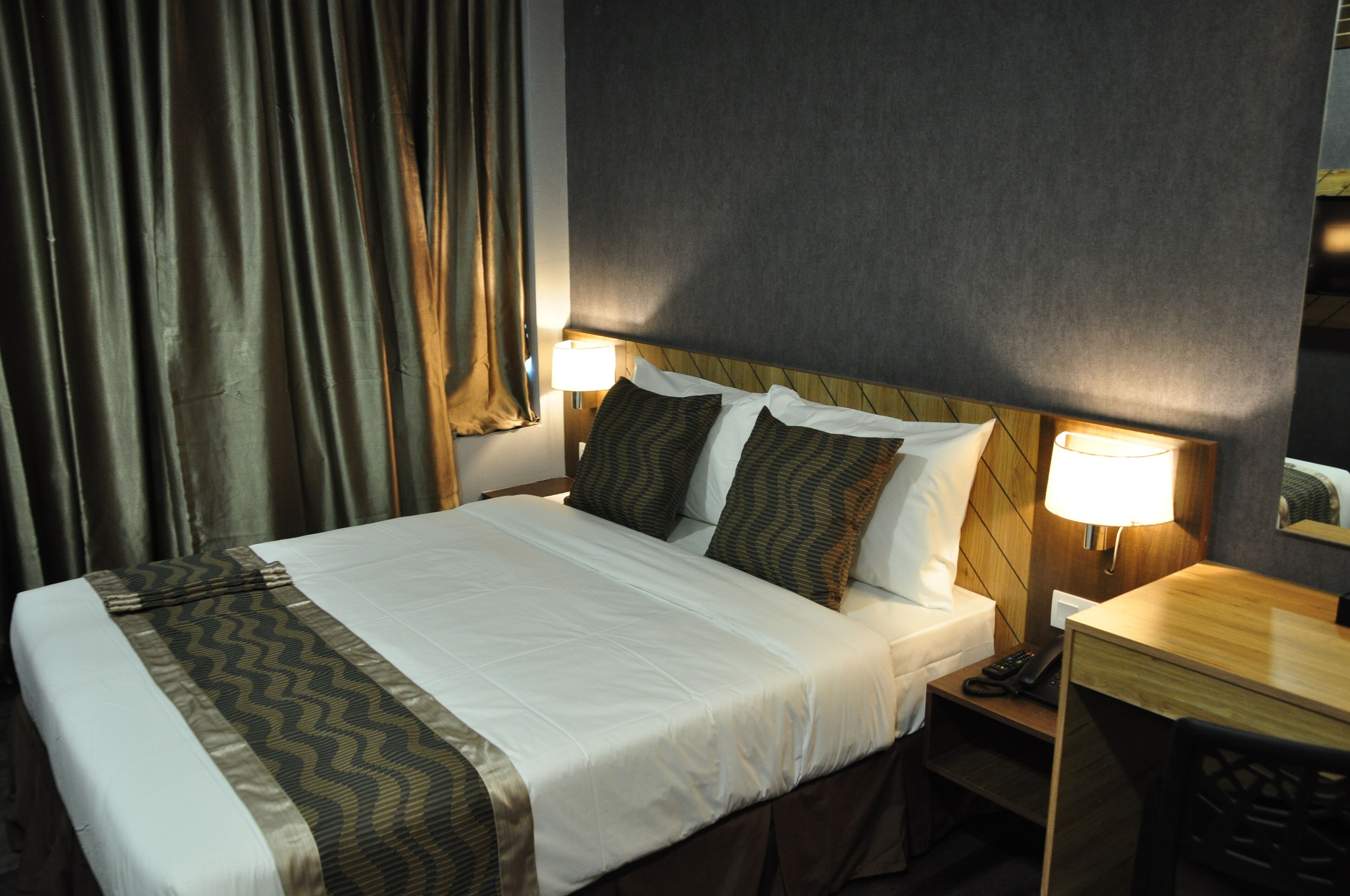 A hotel room with a large bed, two bedside lamps, a wooden nightstand, and a small table.