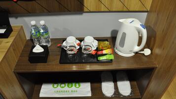 Een houten tafel met een dienblad waarop twee waterflessen, twee glazen, een theezakje, een zakje snacks, een witte waterkoker en een bordje met de tekst 'Laundry Bag' staan.