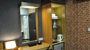 A hotel room with a wooden desk, a mirror, a small refrigerator, and a brick wall. - Valya Hotel - Kuala Terengganu (Kuala Terengganu)