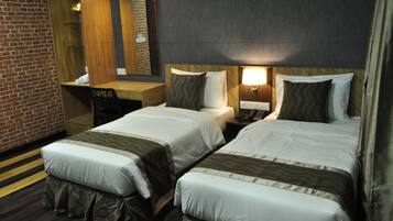 A hotel room with two beds, a desk, a chair, a mirror, and a wall with a brick pattern.