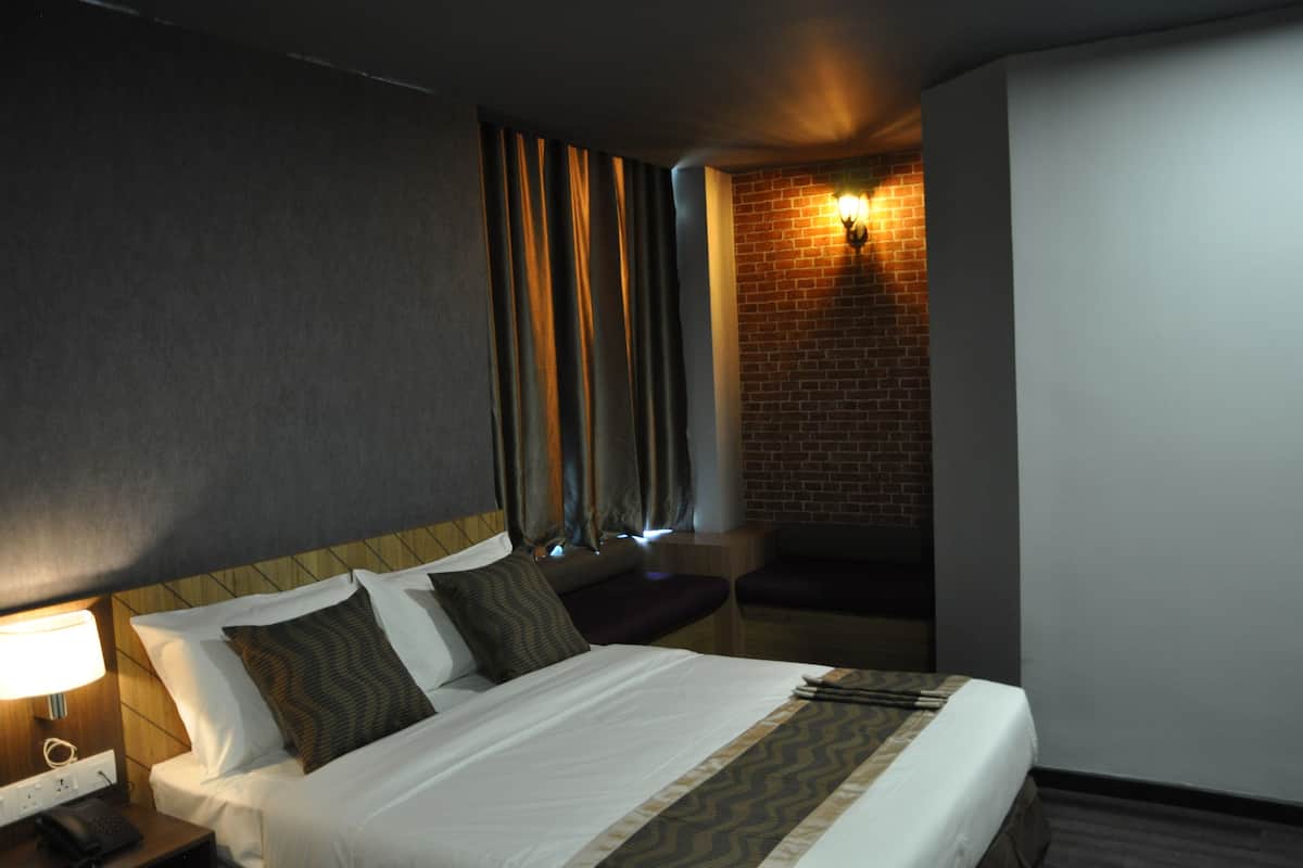 Une chambre d’hôtel avec un grand lit, une table de chevet avec une lampe, un mur en briques et une fenêtre avec des rideaux.