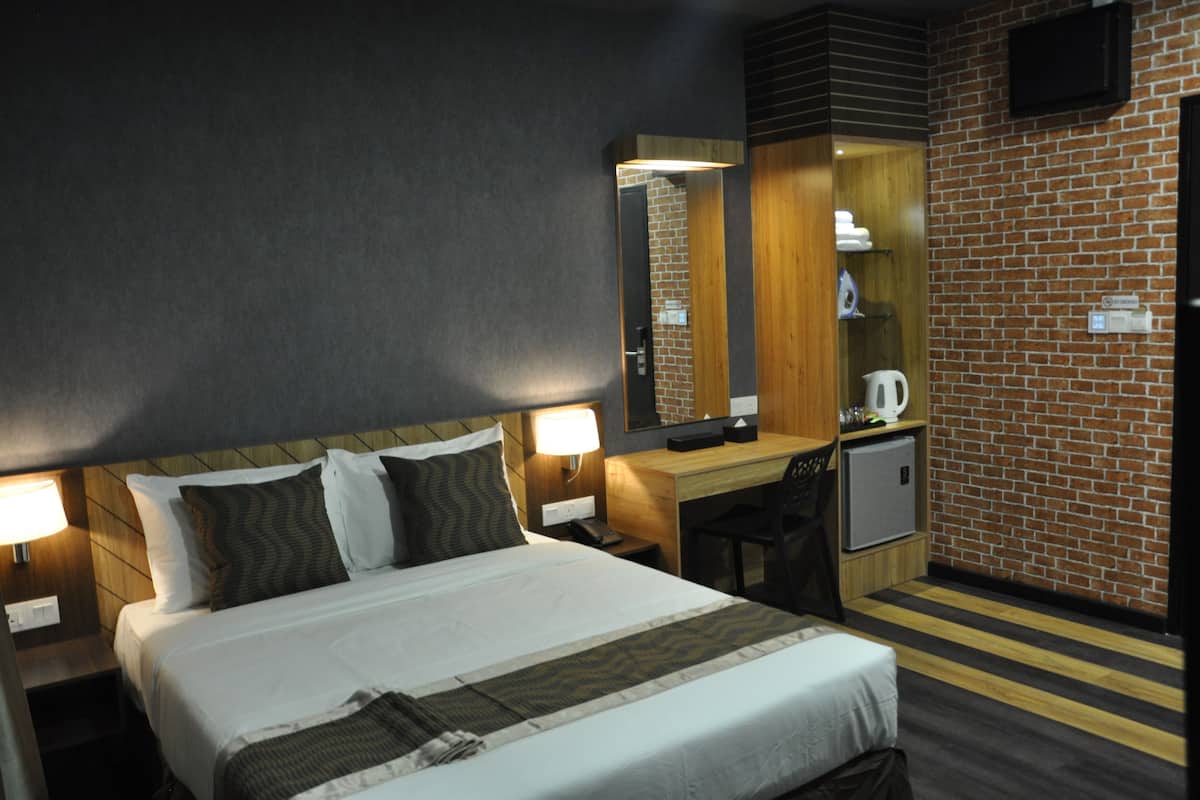 Une chambre d’hôtel équipée d’un lit, d’une table de chevet, d’une lampe, d’un bureau, d’une chaise et d’un petit réfrigérateur.