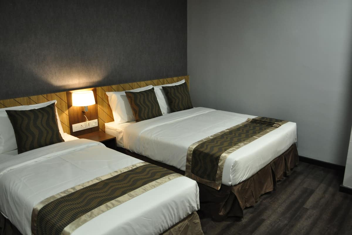 Une chambre d’hôtel avec deux lits, une table de chevet avec une lampe et un mur de couleur sombre.