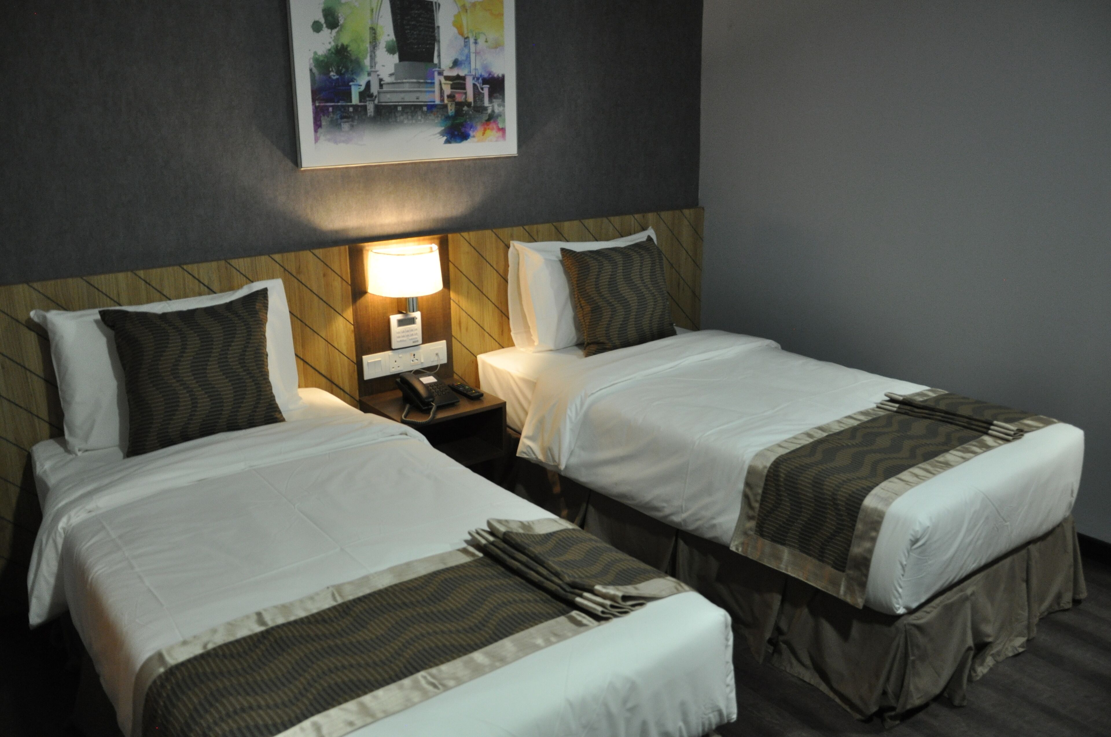 Una habitación de hotel con dos camas individuales, una mesita de noche con lámpara y un cuadro en la pared.