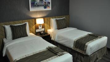 Una habitación de hotel con dos camas individuales, una mesita de noche con lámpara y un cuadro en la pared.