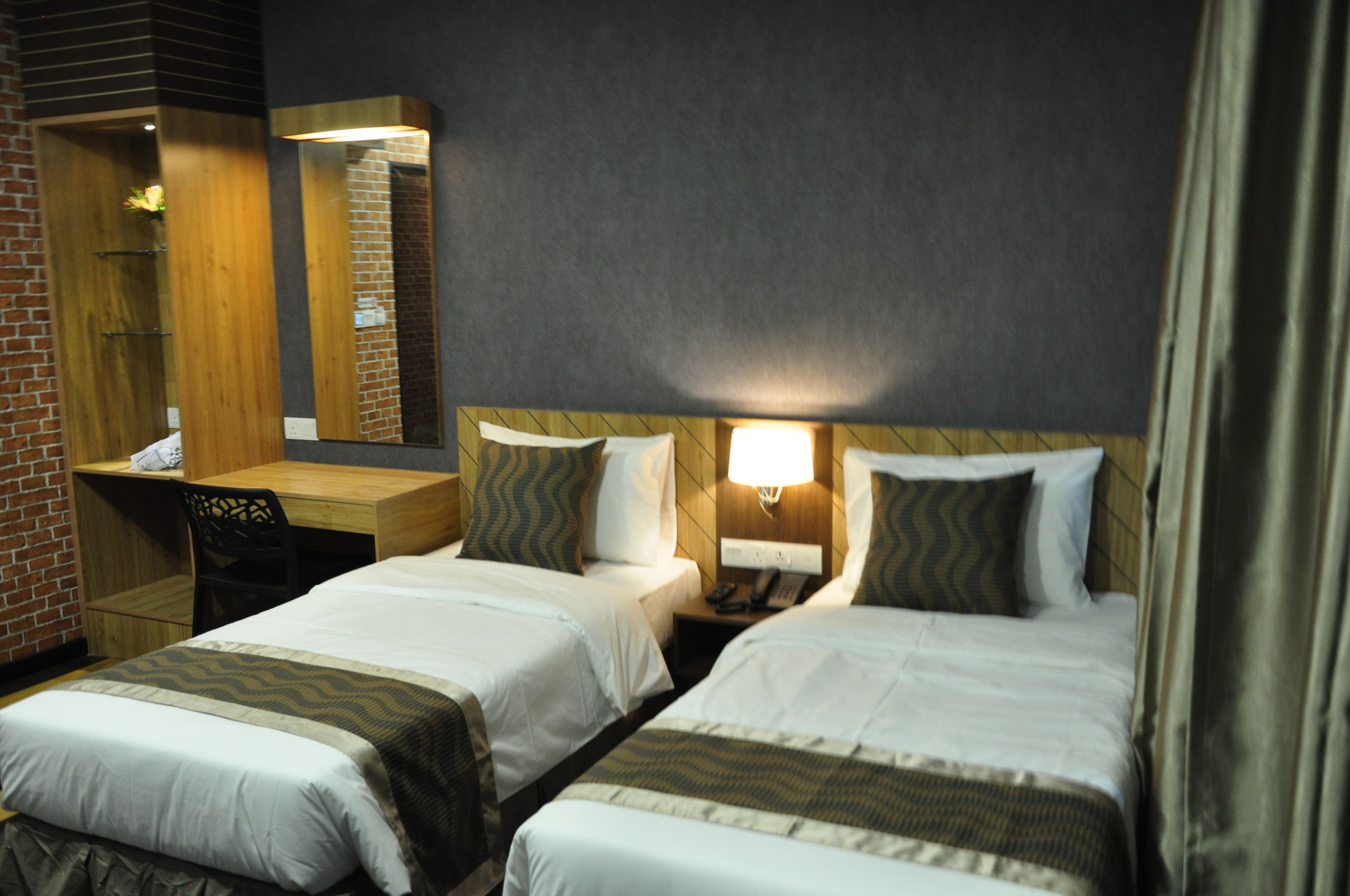 A hotel room with two beds, a desk, a mirror, and a nightstand with a lamp.