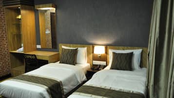 A hotel room with two beds, a desk, a mirror, and a nightstand with a lamp.