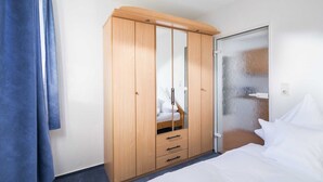 Une chambre d’hôtel avec une armoire en bois, un lit avec du linge de maison blanc et une porte en verre donnant accès à la salle de bain.