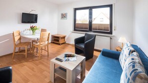 Un salon moderne avec un canapé bleu, des chaises en bois, une table basse, un téléviseur et une fenêtre avec des stores.