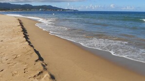 A sandy beach with gentle waves, a clear sky, and distant mountains. - Hai Xia Your Home (New Taipei City)