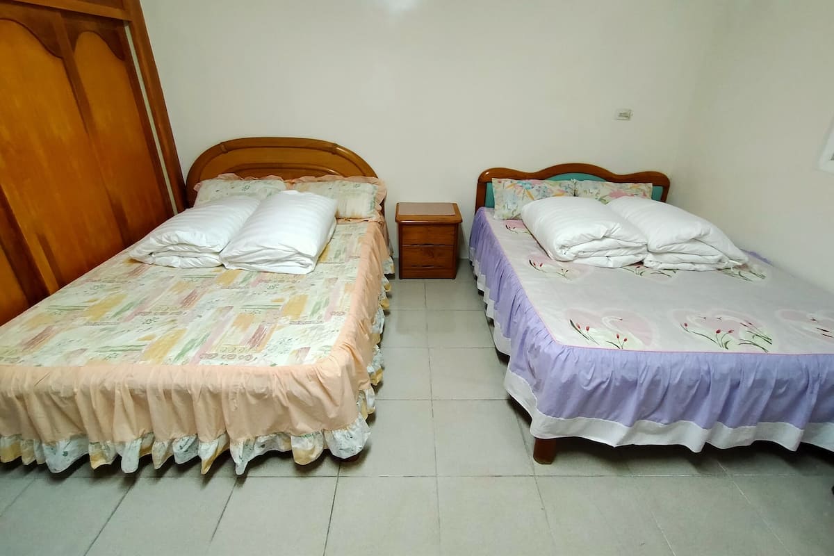 Ein Zimmer mit zwei Einzelbetten, jeweils mit einem hölzernen Kopfteil, einem Nachttisch und einer kleinen Schublade.