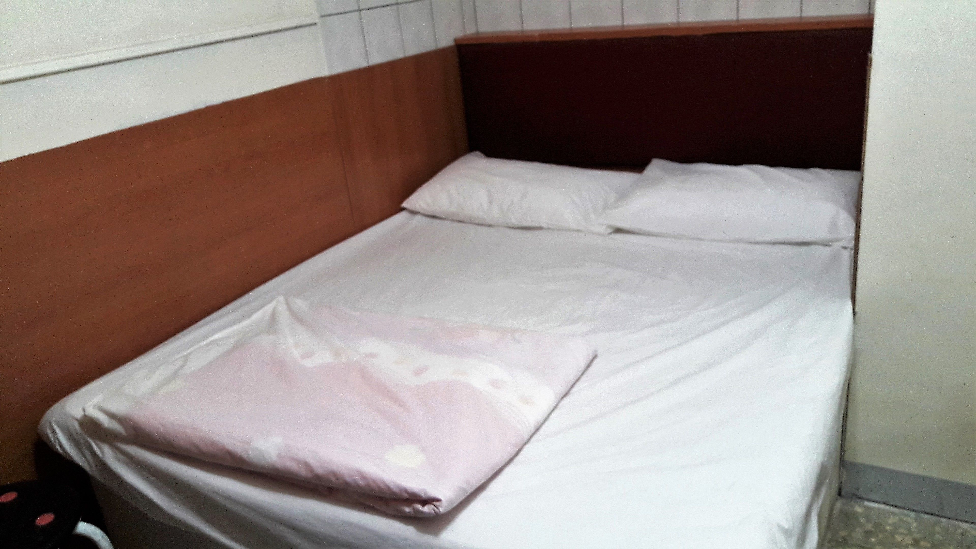 A small, single-bed room with a wooden headboard and white bedding.