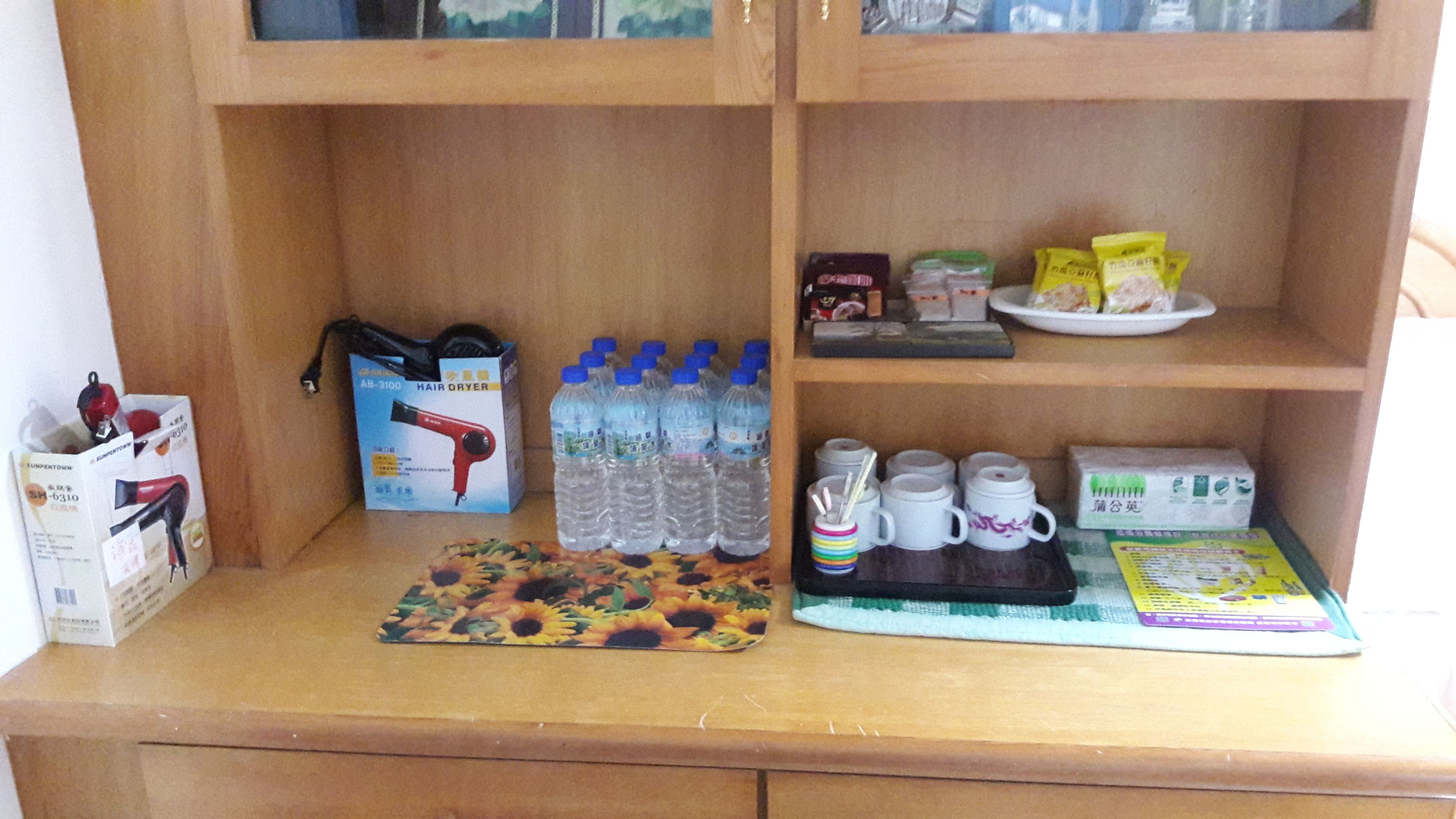Un estante de madera con varios objetos, como un secador de pelo, botellas de agua y una bandeja con tazas y un libro.