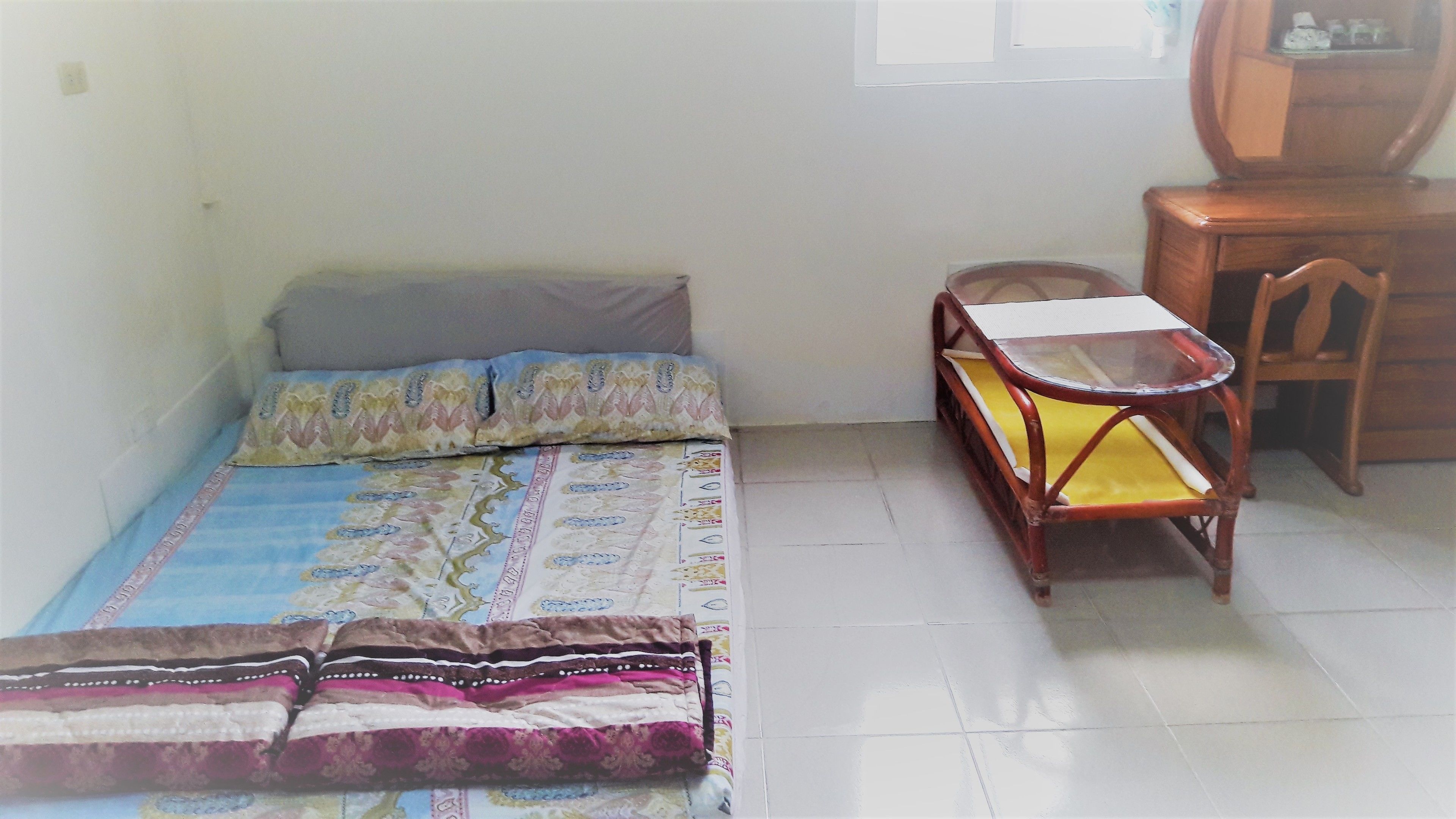 A small, sparsely furnished room with a bed, a small table, and a chair.