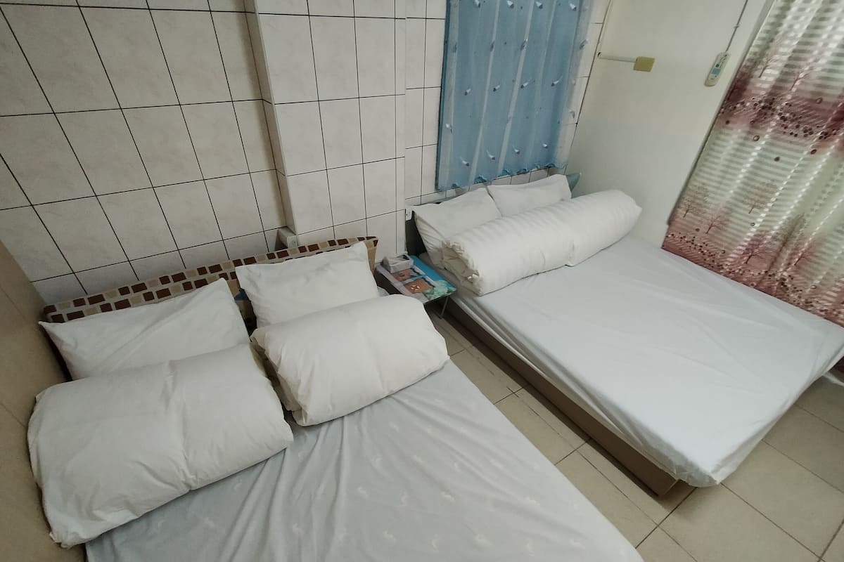 Ein Zimmer mit zwei Betten, jeweils mit weißer Bettwäsche und Kissen. An einer Wand ein blauer Vorhang und hinter den Betten eine geflieste Wand.