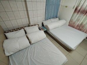 A room with two beds, each with white bedding and pillows. There is a blue curtain on one wall and a tiled wall behind the beds.