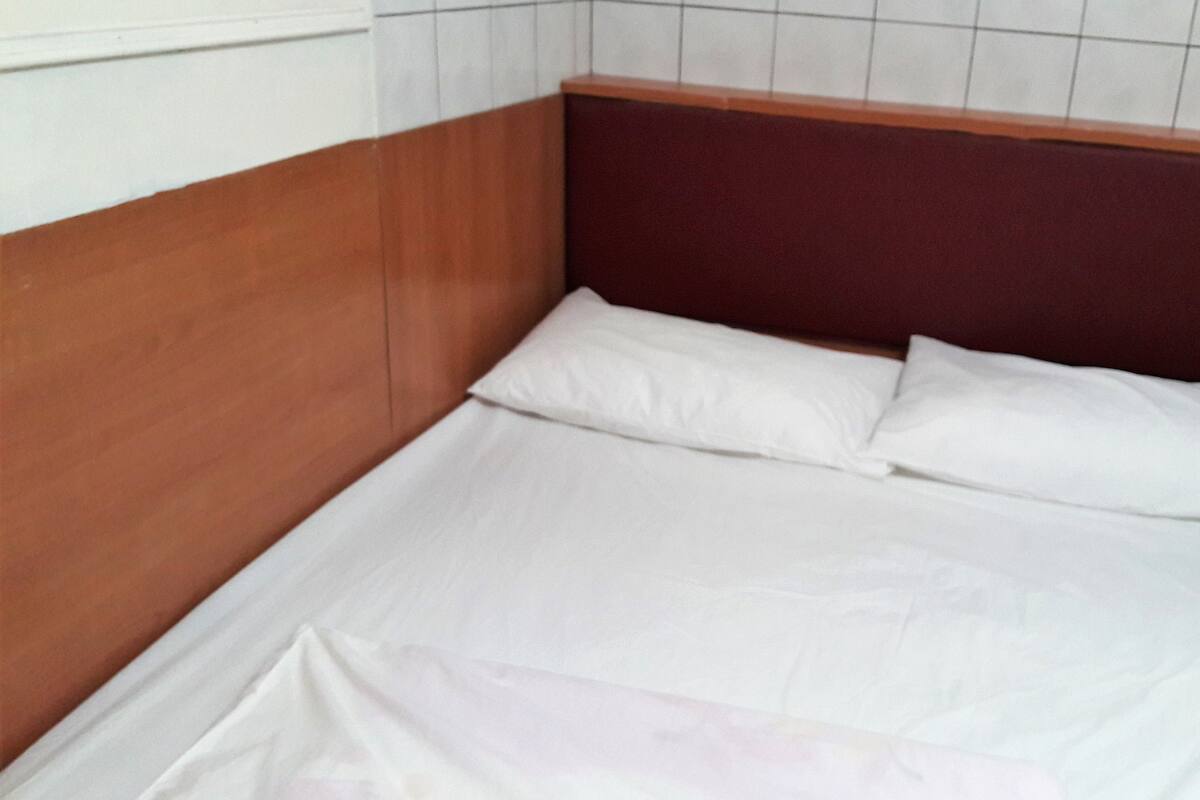 Ein Einzelbett mit weißen Bettwäsche in einem Zimmer, das ein Holz-Kopfteil und weiß geflieste Wände hat.