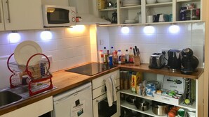 A kitchen with a microwave, dish rack, and various kitchen items on shelves. - Stay in Kings Cross - Flat D (London)