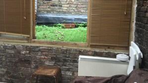 A room with a large window, a brick wall, a radiator, and a small stool. - Stay in Kings Cross - Flat D (London)