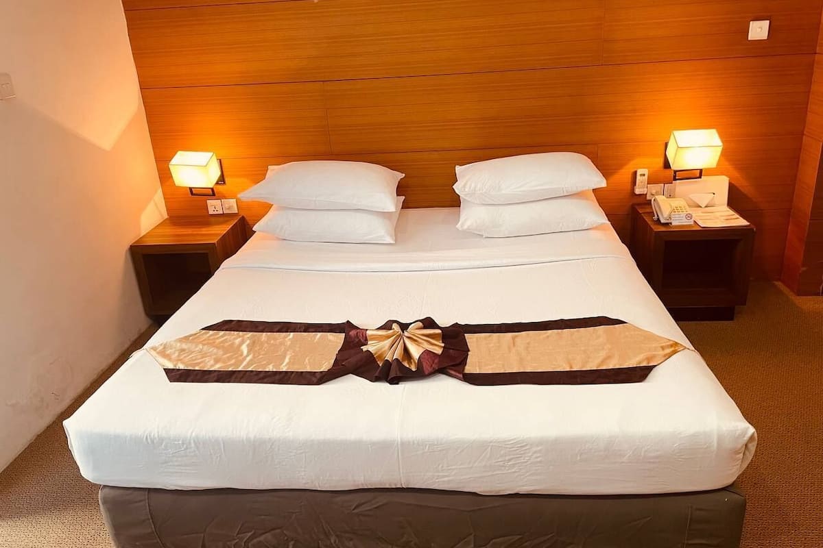 A hotel room with a large bed, two bedside tables, and two wall-mounted lamps.