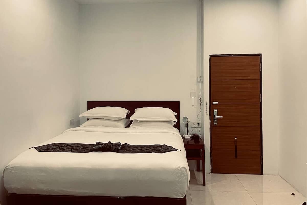 A neatly made bed with white linens and a dark throw blanket, a wooden nightstand with a lamp, and a wooden door with a handle.