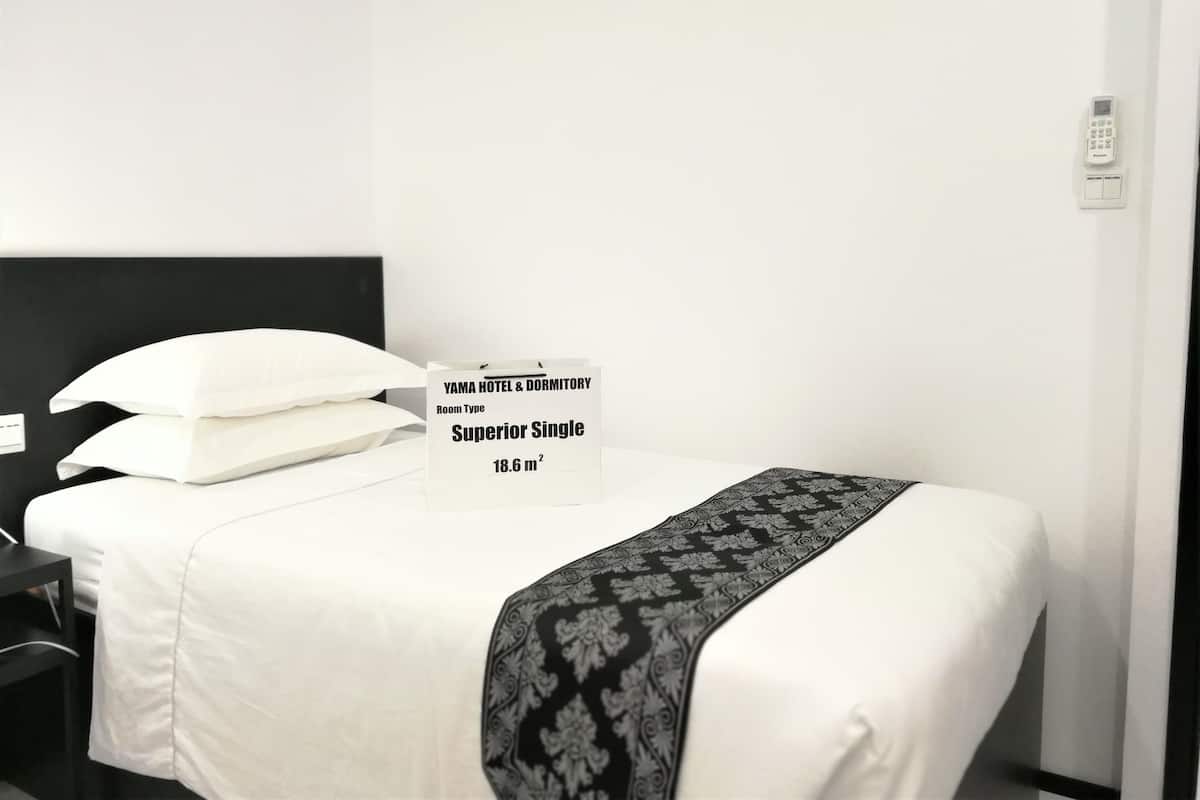 A hotel room with a bed, white bedding, a black headboard, a bedside table, and a sign indicating the room type as 'Superior Single' with an area of 18.6 m².